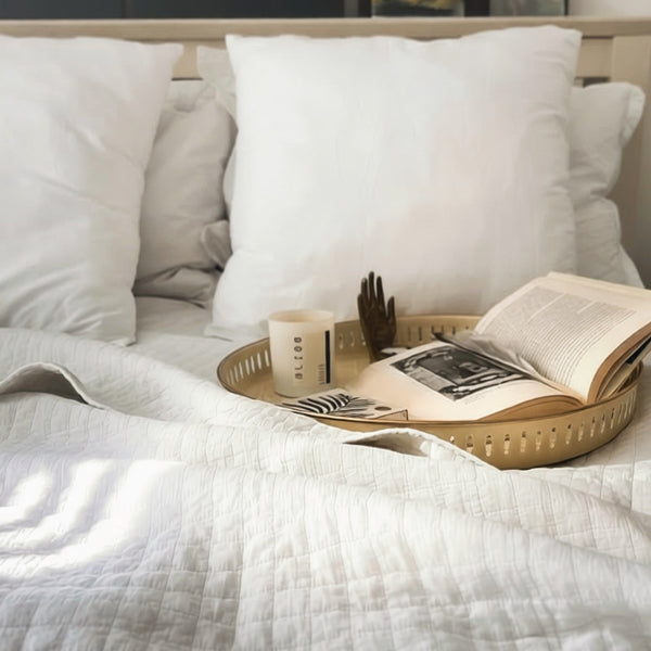 Bed with white bedding and pillows, a tray with a book and candle.