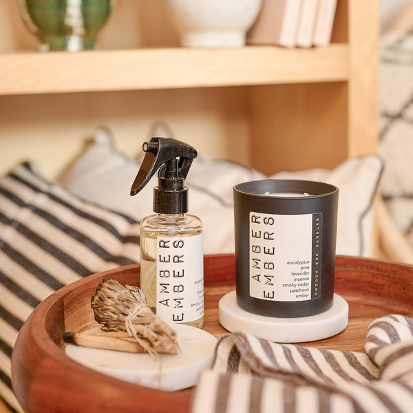 Ambers Embers candle and spray bottle on a wooden tray with striped pillows in the background