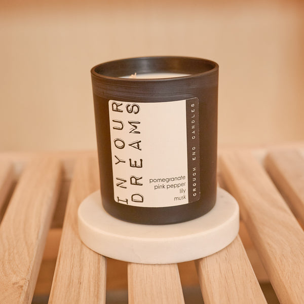 Candle in a black container with a label on a wooden surface