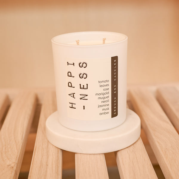 Candle labeled 'HAPPINESS' on a wooden stand with a warm background