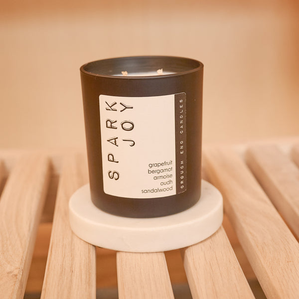 Candle with 'Spark Joy' label on a wooden stool against a beige background