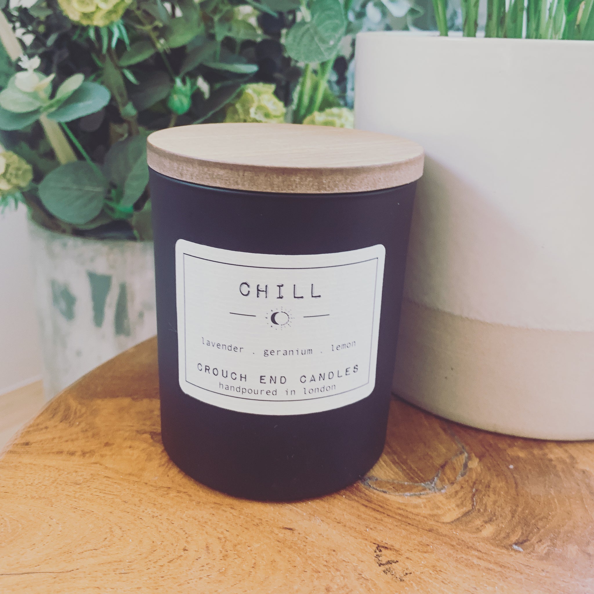 a black soy wax candle with a wooden lid, the cream  label says "Chill" lavender, geranium and lemon 
